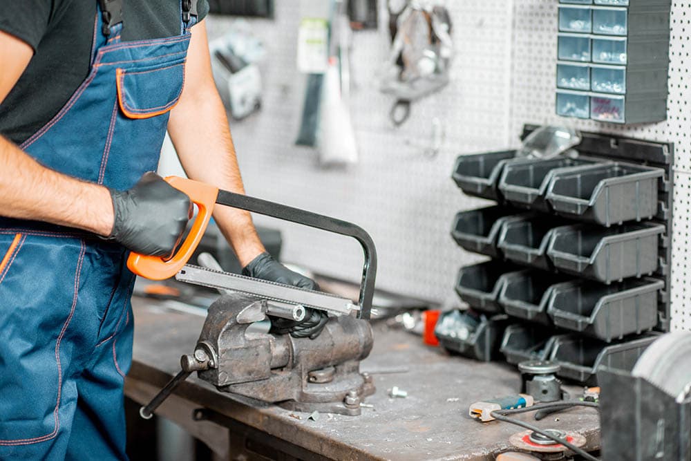 Handyman in overalls cutting metal tube with hacksaw