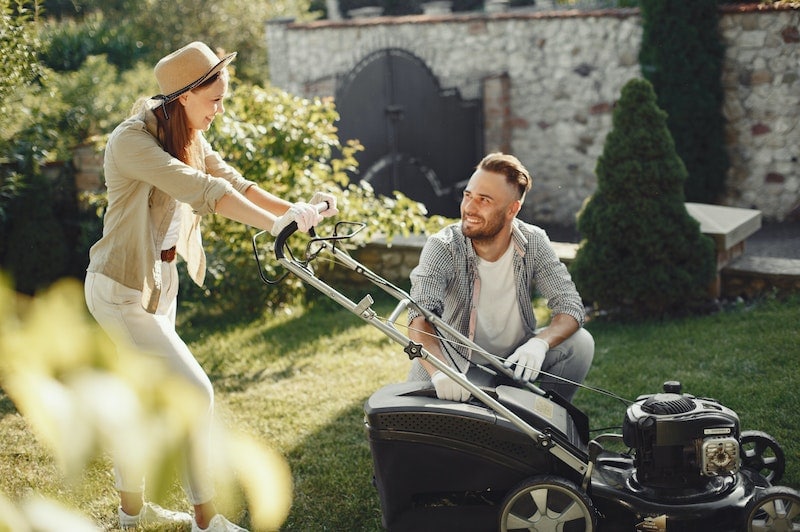 Two persons holding a lawn mower
