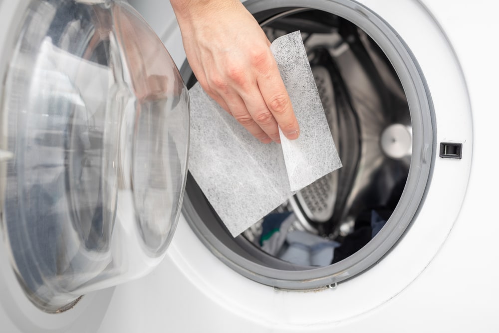 hand putting dryer sheet in the laundry machine