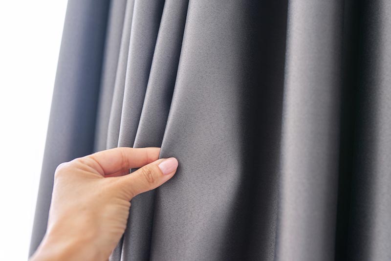 woman's hand touching gray blackout curtain