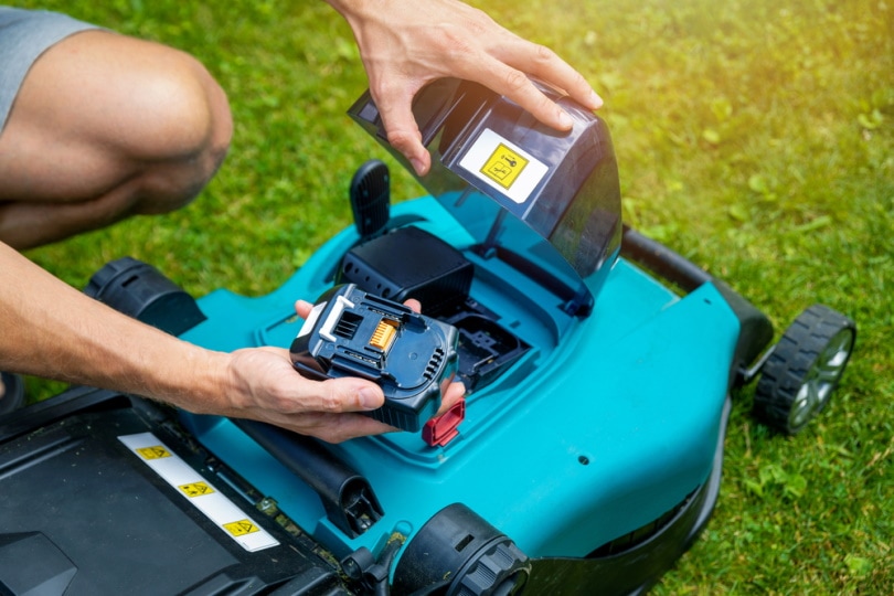 man putting battery on lawn mower
