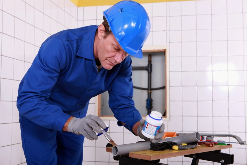 plumber applying glue to grey pipe